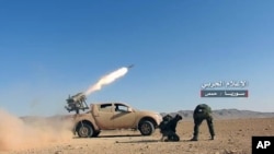 FILE - May 25, 2017 photo provided by the government-controlled Syrian Central Military Media, shows Syrian government troops firing multiple launcher rockets at insurgent group's position, in the Syrian province of Homs.