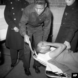 Thomas Hagan, 22, is carried in police custody from Jewish Memorial Hospital en route to Bellevue Hospital in New York, Feb. 21, 1965.