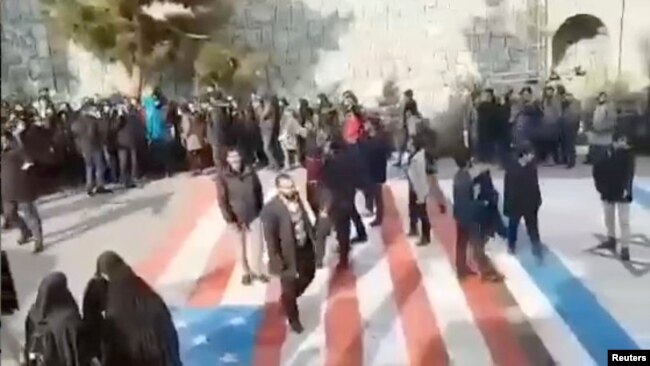 Algunas personas caminan sobre las banderas de Estados Unidos e Israel en la Universidad Shahid Beheshti de Teheran el 12 de enero de 2020, mientras que otras dan la vuelta alrededor, en esta foto de Reuters tomada de un video en las redes sociales.
