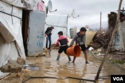 Hassan Fahd al Raja, holding a bucket, helps his siblings drain water out of their family's tent, which is part of a refugee camp in Lebanon's Bekaa valley. (Photo: John Owens for VOA)