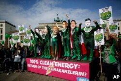 Climate activists in green costumes and with masks of the G7 leaders attend a protest in front of the Brandenburg Gate near a building hosting the 'Petersberg Climate Dialogue' conference in Berlin, Germany.