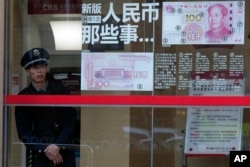 A security guard looks out near a display showing the security features of the new 100 Yuan note in Beijing, China, Jan. 7, 2016.