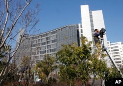 FILE - A cameraman on a ladder stands by outside Tokyo Detention Center, where former Nissan chairman Carlos Ghosn and former another executive Greg Kelly are being detained, in Tokyo, Dec. 21, 2018.