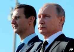 FILE - Russian President Vladimir Putin, right, and Syrian President Bashar al-Assad watch troops marching at the Hemeimeem air base in Syria, Dec. 11, 2017.