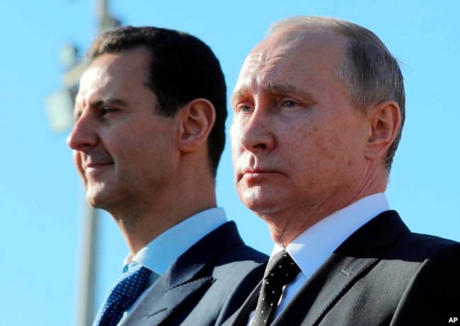 FILE - Russian President Vladimir Putin, right, and Syrian President Bashar al-Assad watch troops marching at the Hemeimeem air base in Syria, Dec. 11, 2017.