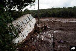 A van is seen in half buried in the mud after a dam collapse near Brumadinho, Brazil, Jan. 26, 2019. Rescuers in helicopters on Saturday searched for survivors while firefighters dug through mud in a huge area in southeastern Brazil buried by the collapse.