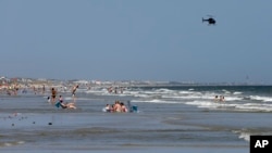 A helicopter flies close to the water as vacationers relax on the beach in Oak Island, North Carolina, June 15, 2015.