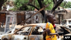 FILE - Two boys stand in front of burnt cars in Michika, a city recaptured from Boko Haram by the Nigeria military. 