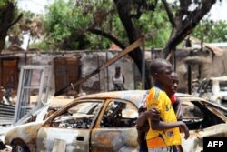 FILE - Two boys stand in front of burnt cars in Michika, a city recaptured from Boko Haram by the Nigeria military early this year, May 10, 2015.