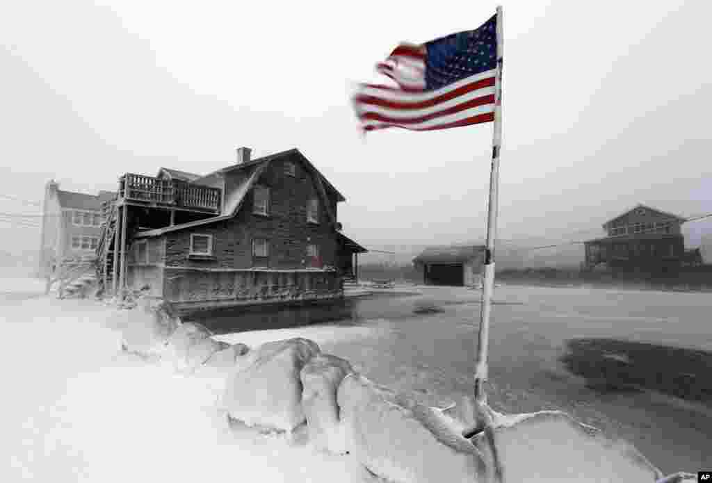 A tattered flag flies by a flooded yard along the shore in Scituate, Massachusetts, Jan. 3, 2014. A blustering winter storm dropped nearly two feet of snow just north of Boston.