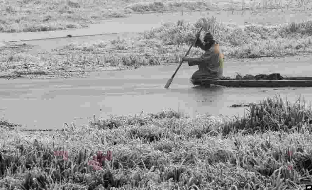 Seorang pria Kashmiri berusaha melewati air danau yang membeku pada pagi hari yang dingin dan berkabut di Srinagar, India.