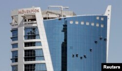 FILE - Cleaners wash the glass windows of the Movenpick Hotel in Doha, Qatar.