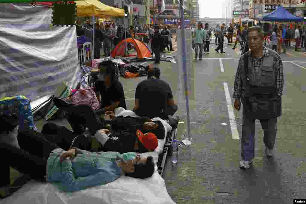 Seorang warga berjalan melewati demonstran pro-demokrasi yang sedang beristirahat ketika menduduki sebuah jalanan di pusat perbelanjaan Hong Kong, Mong Kok, 19 November 2014.