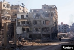 FILE - Men ride a motorbike past buildings damaged by what activists said was shelling by forces loyal to Syria's President Bashar al-Assad in Daraya, Jan. 15, 2014.
