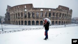 A man stands in front of the ancient Colosseum blanketed by the snow in Rome, Feb. 26, 2018. 