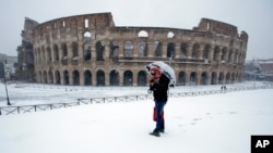 A man stands in front of the ancient Colosseum blanketed by the snow in Rome, Feb. 26, 2018. 