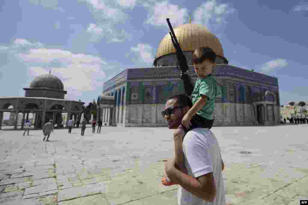 Seorang pria Palestina memanggul seorang anak kecil yang memegang senapan mainan di luar Kubah Batu di kompleks Masjid Al-Aqsa di kota Yerusalem.