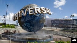 FILE - Park guests relax and cool off with a water mist under the globe at Universal Studios City Walk in Orlando, Fla.