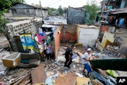 A member of the Philippine National Police SWAT team walks through debris as former inhabitants try to salvage any items following the demolition of their community Monday, June 6, 2016 in suburban Quezon city northeast of Manila, Philippines.