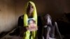 Rachel Daniel, 35, holds up a picture of her abducted daughter Rose Daniel, 17, as her son Bukar, 7, sits beside her at her home in Maiduguri, Nigeria, May 21, 2014. 