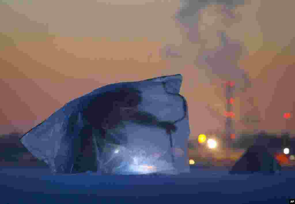 A man covered with a plastic bag for protection from the wind and cold, fishes through an ice hole in the Finnish Gulf west of St.Petersburg, Russia, March 1, 2016.