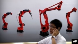 FILE - In this Aug. 15, 2018, file photo, a visitor talks on his smartphone in front of a display of manufacturing robots from Chinese robot maker Honyen at the World Robot Conference in Beijing, China. China will make economic changes at its own pace regardless of U.S. pressure, and their worsening dispute over technology policy can only be solved through negotiations as equals, a Commerce Ministry spokesman said Thursday, Aug. 30, 2018.