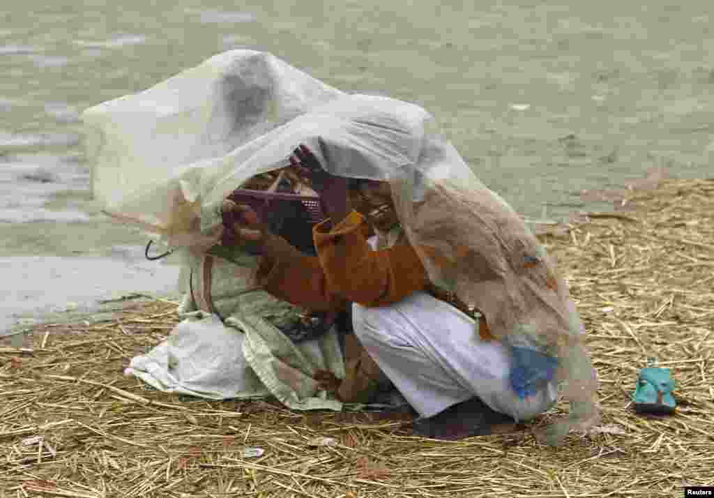 Girls use a plastic sheet to protect themselves from rain on the banks of River Ganges in the northern Indian city of Allahabad.