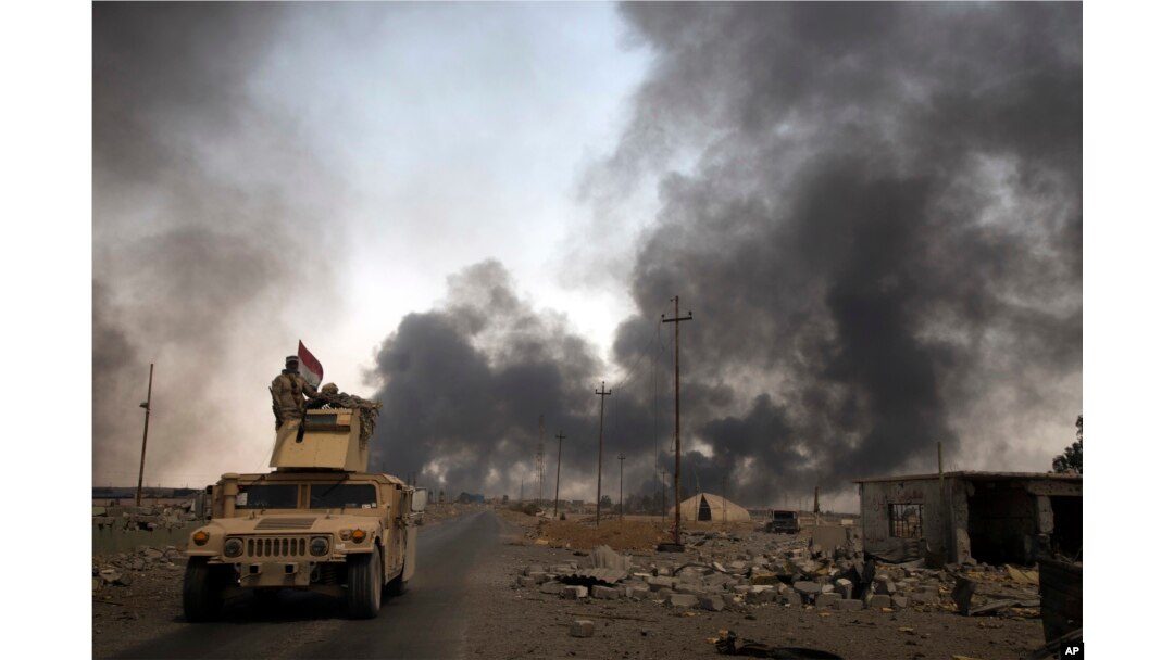 FILE - Iraqi security forces patrol as smoke rises from burning oil wells in Qayara, south of Mosul, Iraq, Aug. 31, 2016.