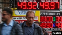People walk along a street past a display showing currency exchange rates in Moscow, Sept. 29, 2014.