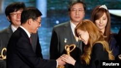 韩国流行歌曲女团“少女时代”的队长金泰妍（右二，Taeyeon）从韩国总理手里接过“总理表彰奖”。这个奖表扬“少女时代”对世界推广“韩流”的努力（2011年11月21日））