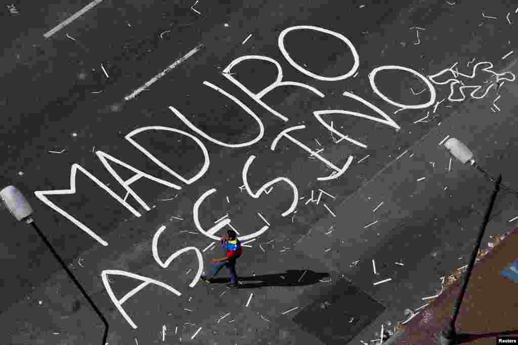 An opposition supporter walks past words painted on a blocked street, reading &#39;Maduro murderer&#39;, at Altamira Square in Caracas, Feb. 21, 2014. 