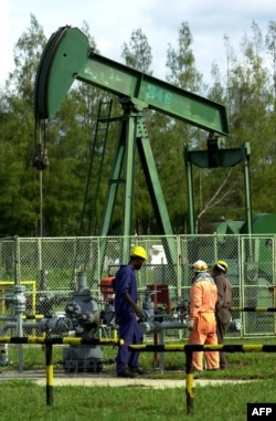 FILE - Workers working in front of one of the Bruneian Shell's oil well pumps in Seria, Brunei, Nov. 16, 2000.