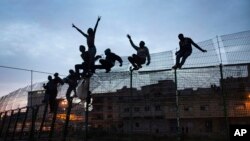 FILE - Sub-Saharan migrants climb over a metallic fence that divides Morocco and the Spanish enclave of Melilla, March 28, 2014. 