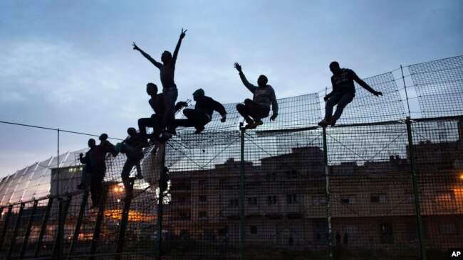 FILE - Sub-Saharan migrants climb over a metallic fence that divides Morocco and the Spanish enclave of Melilla, March 28, 2014. 