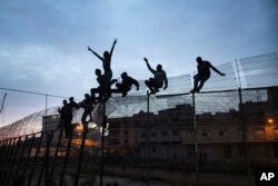 FILE - Sub-Saharan migrants climb over a metallic fence that divides Morocco and the Spanish enclave of Melilla, March 28, 2014.