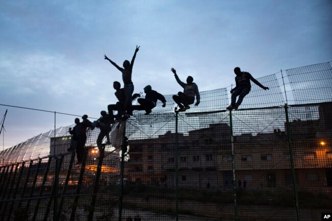 FILE - Sub-Saharan migrants climb over a metallic fence that divides Morocco and the Spanish enclave of Melilla, March 28, 2014.