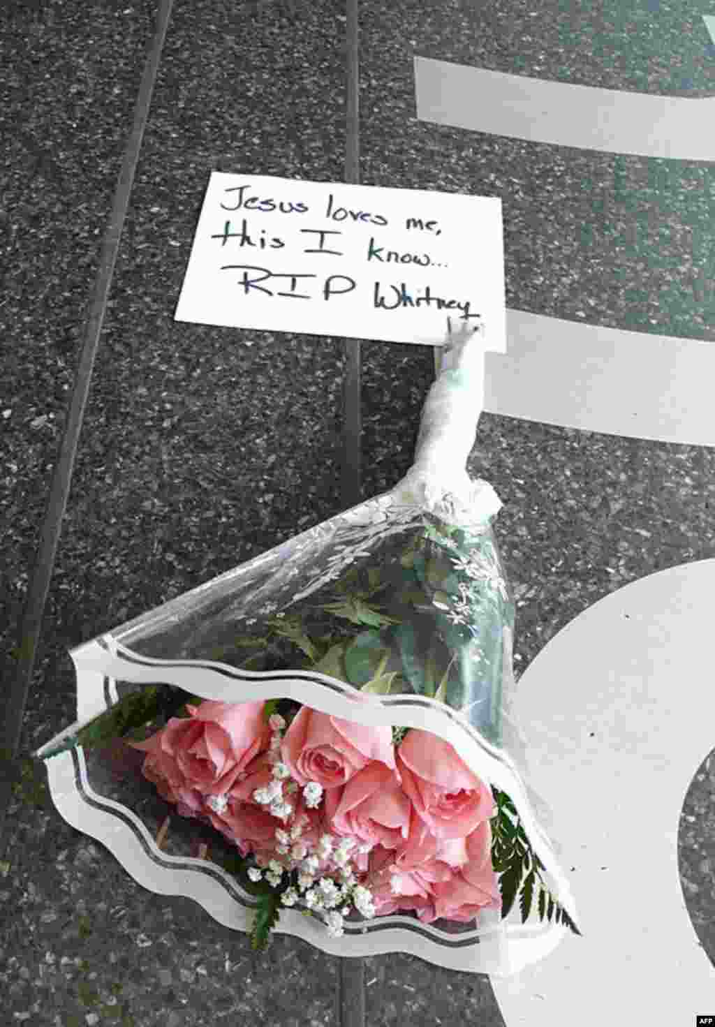 Букет рожевих троянд та поштівка біля входу до будівлі Apollo Theater. На поштівці текст з пісні, яку Г'юстон виконала останньою у житті :"Yes, Jesus Loves Me." Співачка померла 11-го лютого 2012-го року у віці 48-ми років у Лос-Анджелесі.. (AP)