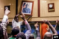 People remove from the wall at the International Conference center, where parliament had their sitting, the portrait of former Zimbabwean President Robert Mugabe after his resignation, Nov. 21, 2017, in Harare.