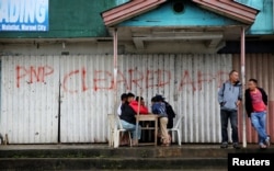 Residents play chess in front of a closed establishment with a sign declaring the area cleared by government troops inside Marawi city, southern Philippines, Oct. 18, 2017.