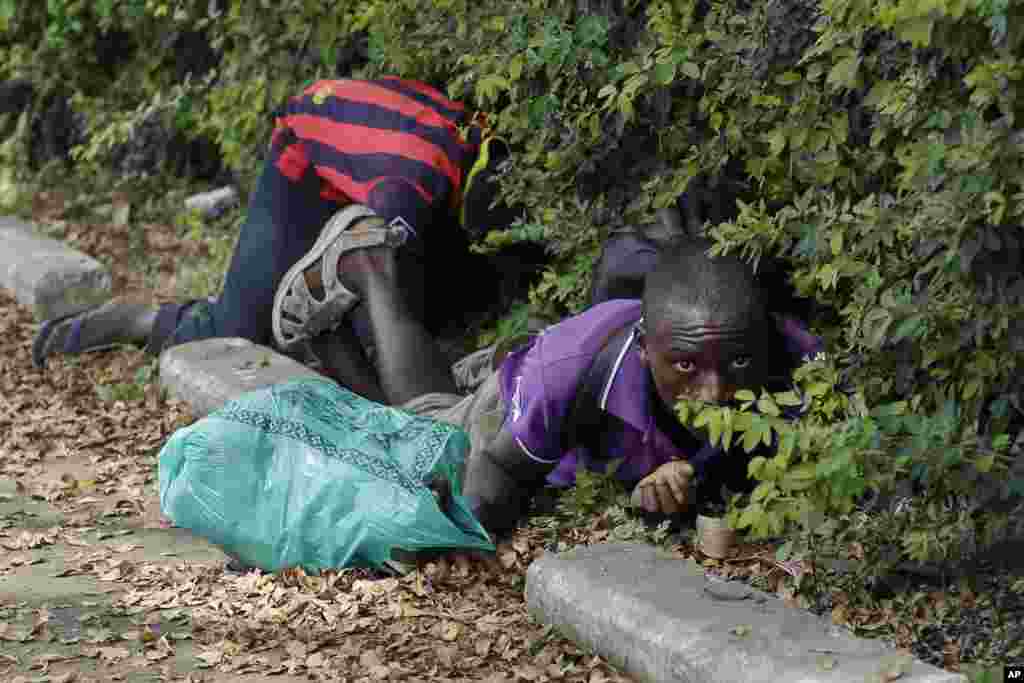 Homens escondem-se por baixo de arbustos para se protegerem de tiros, em Bujumbura, Burundi.