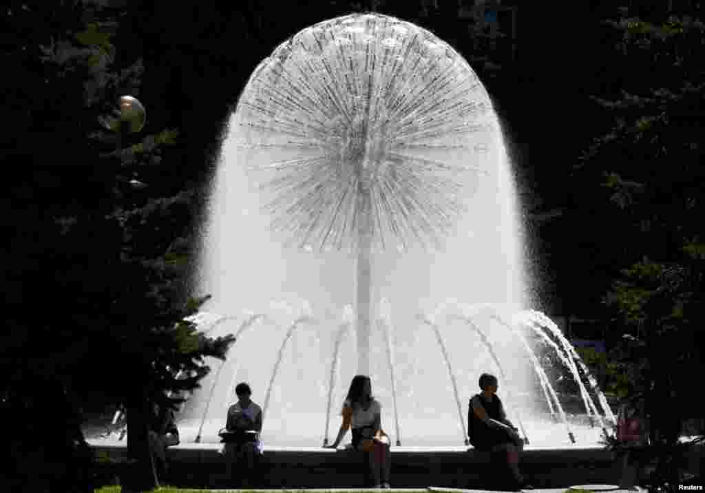 People sit next to a fountain in central Kyiv, Ukraine.