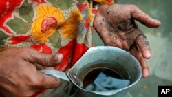 FILE - Hanufa Bibi, 45, holds a can full of contaminated well water, at her village in Chandipur, about 120 kilometers (75 miles) east of Dhaka, Bangladesh, Feb. 22, 2010.