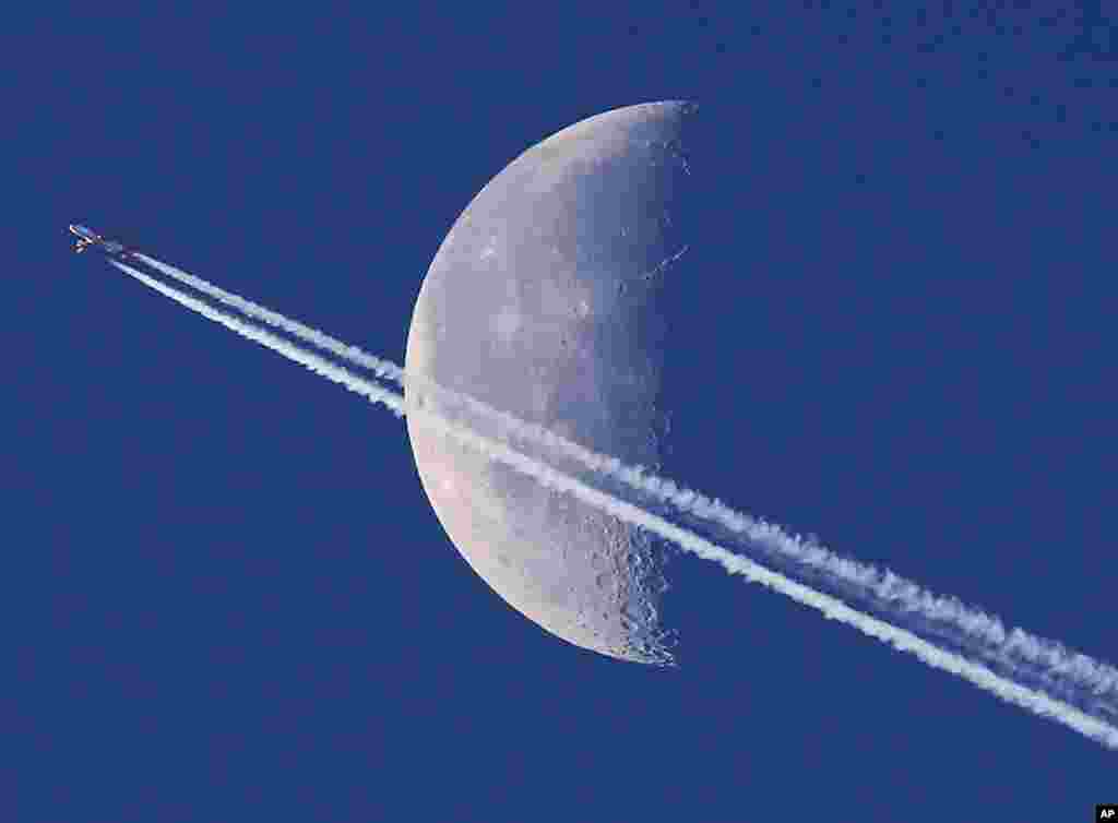 An aircraft leaves a trail in the sky as it passes the moon over Frankfurt, Germany.