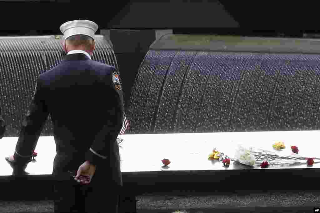 Petugas pemadam kebakaran menyentuh nama para koleganya yang tewas dalam serangan 9/11, dalam upacara di World Trade Center di Memorial Nasional 11 September di New York (11/9). (AP/Mary Altaffer)