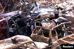 FILE - Indonesian forensic policemen walk past destroyed cars near the site of the Oct. 12, 2002, bomb blasts at Kuta on Indonesia's resort island of Bali, Oct. 18, 2002.