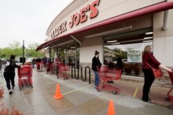 FILE - Customers observe social distancing as they wait to be allowed to shop at a Trader Joe's supermarket in Omaha, Neb., May 7, 2020.