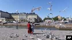 Tourists feed sea gulls in front of the Presidential palace in Helsinki, Finland, Thursday, June 28, 2018. (Onni Ojala/Lehtikuva via AP)