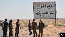 FILE - This photo released Sept 3, 2017 by the Syrian official news agency SANA, shows Syrian troops and pro-government gunmen standing next to a placard in Arabic which reads, "Deir el-Zour welcomes you," in the eastern city of Deir el-Zour, Syria. 