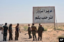 This photo released Sept 3, 2017 by the Syrian official news agency SANA, shows Syrian troops and pro-government gunmen standing next to a placard in Arabic which reads, "Deir el-Zour welcomes you," in the eastern city of Deir el-Zour, Syria.