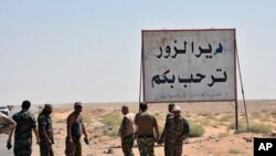 This photo released Sept 3, 2017 by the Syrian official news agency SANA, shows Syrian troops and pro-government gunmen standing next to a placard in Arabic which reads, "Deir el-Zour welcomes you," in the eastern city of Deir el-Zour, Syria. 